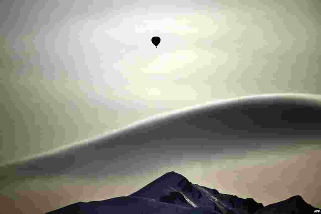 This photograph taken from Cordon ski resort near Megeve near Cordon ski resort near Megeve, shows a hot air balloon drifting over the Massif du Mont-Blanc mountains range in the French Alps in France.