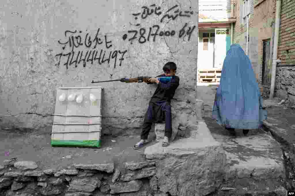 An Afghan burqa-clad woman (R) walks past a boy playing with an air gun in Kabul.
