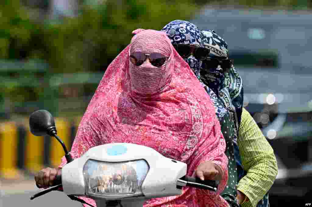 Women cover their faces with a cloth while riding a two-wheeler on a hot day, in Raipur, India.