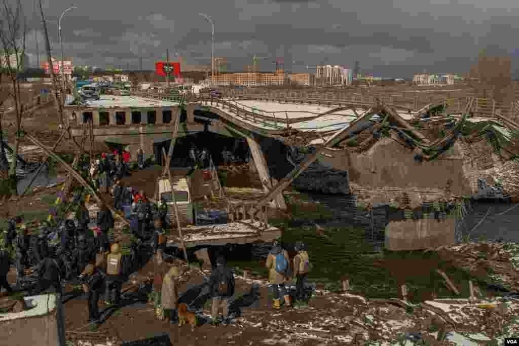 Civilians that were trapped in Irpin escape from the battles through an improvised path created alongside a bombed bridge by Ukrainian forces, in Ukraine, March 8, 2022. (Yan Boechat/VOA)