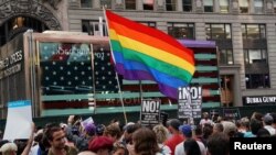 FILE - A rainbow flag flies as people protest U.S. President Donald Trump's announcement that he planned to reinstate a ban on transgender individuals from serving in any capacity in the U.S. military, in Times Square, in New York, July 26, 2017. 