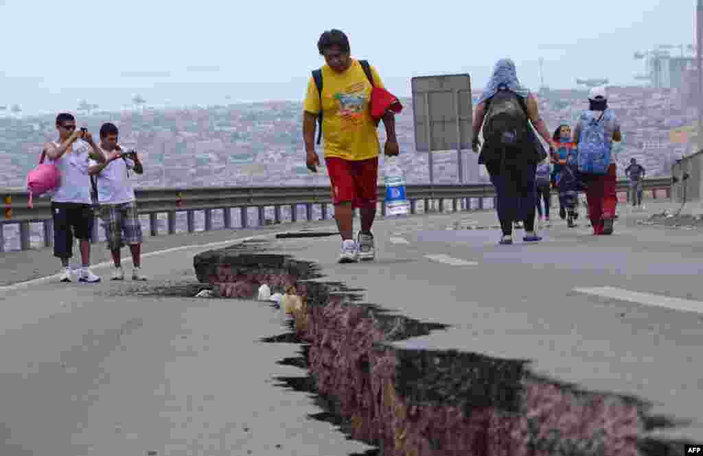 Warga Chile berjalan di sebuah jalan yang rusak akibat gempa di kota Iquique, Chile utara, sehari setelah gempa 8.2 skala Richter melanda Chile. 