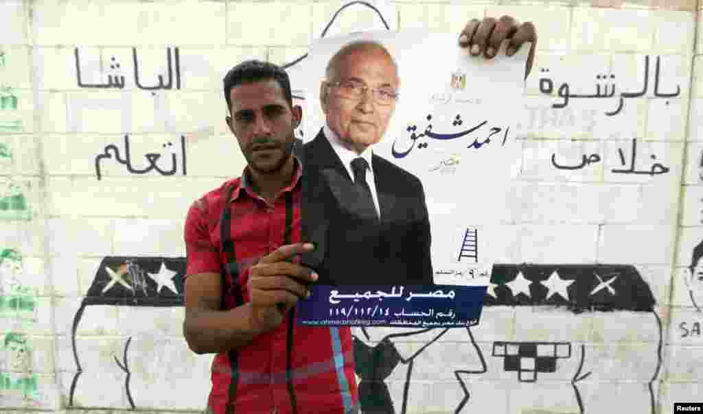 An Egyptian man holds a poster of former prime minister and presidential candidate Ahmed Shafiq, with Arabic that reads " Egypt for all", in front of a wall sprayed with anti-police graffiti in Cairo, May 22, 2012.