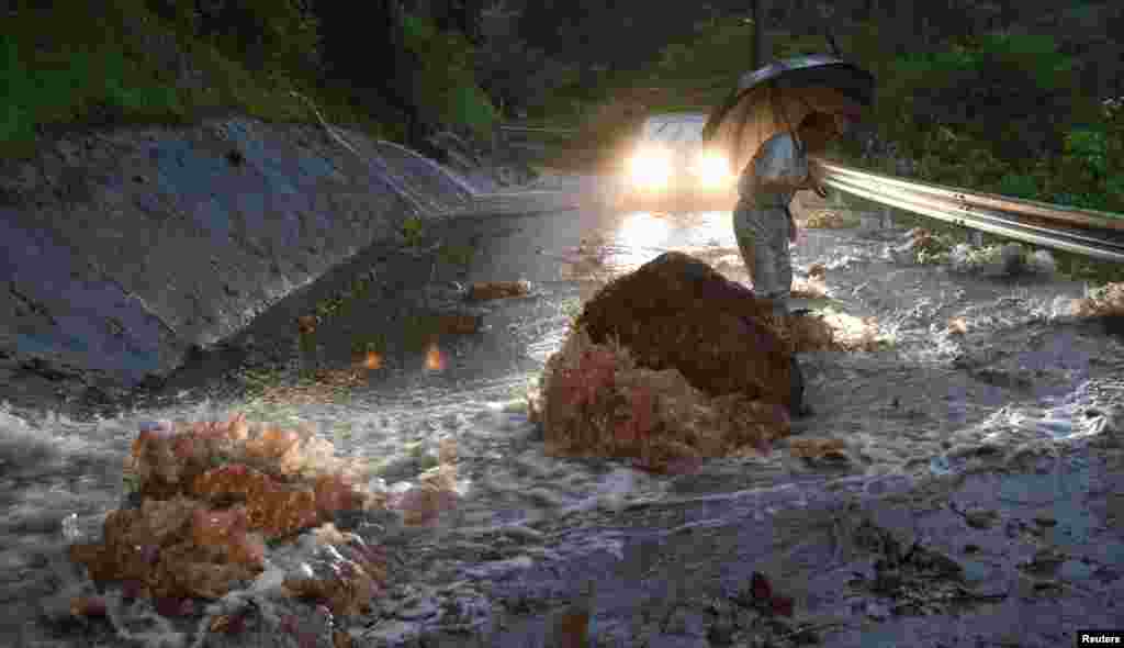 A man crosses a flooded road with fallen rocks in Hita in Oita Prefecture, Japan, after torrential rain hits, in this photo taken by Kyodo.