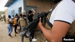 FILE - A member of Honduras' Police Anti Maras and Gangs Against Organized Crime Directorate stands guard as other directorate members frisk people in Tegucigalpa, Honduras, Nov. 26, 2022. 