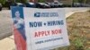 A now hiring sign stands in the parking lot of the University Hills branch of the United States Postal Service, Oct. 12, 2021, in southeast Denver. 