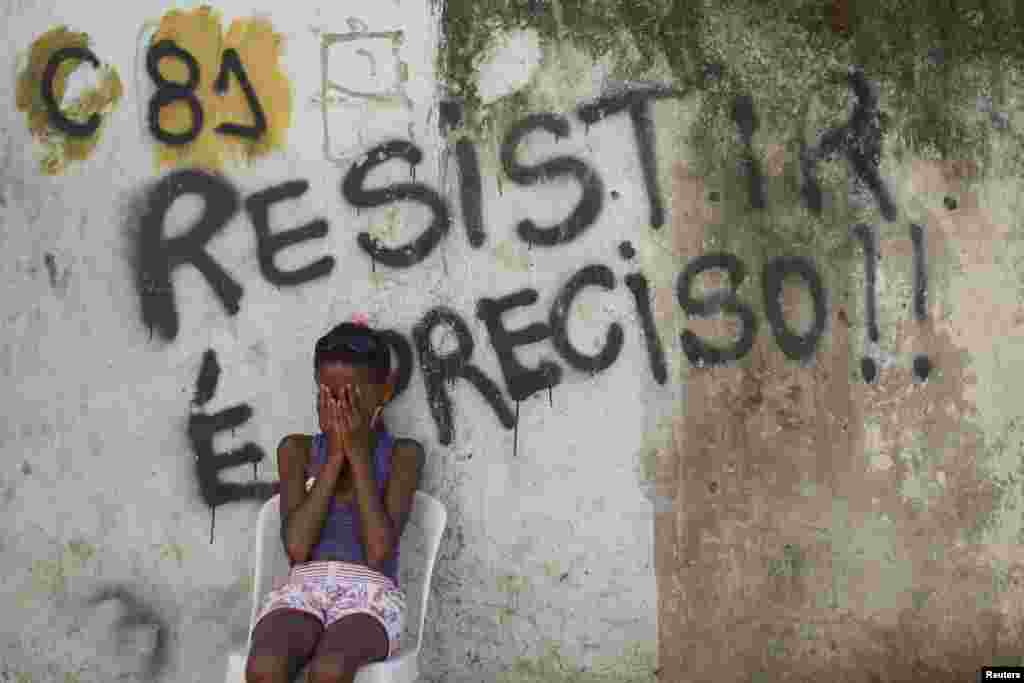 A girl sits in front of a wall with graffiti that reads, "We must resist," in Metro slum near Maracana stadium in Rio de Janeiro. Residents are protesting eviction from their homes. The removal of the community is part of the renovation works of the area for the 2014 World Cup.