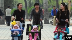 FILE - Women push babies in strollers through a Beijing park during a public holiday.