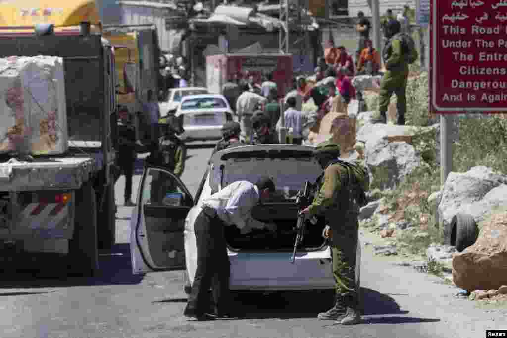 Seorang tentara Israel mencari kendaraan Palestina di sebuah post pemeriksaan dekat Tepi Barat kota Hebron, 15 Juni 2014.