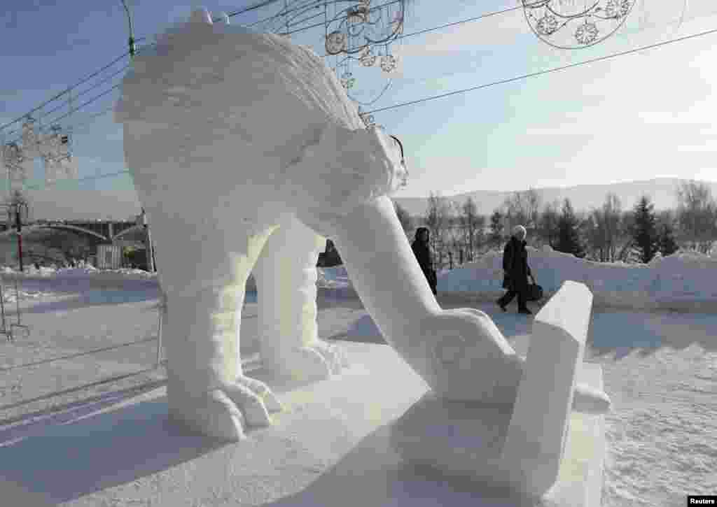 Para pejalan kaki berjalan melewati patung salju "Computeriada" yang dibuat oleh "Tim Latvia" dari Pavilosta, dalam "Festival Es Ajaib Siberia" di tepi Sungai Yenisei di Krasnoyarsk, Rusia. Lebih dari 20 tim pematung es dan salju yang mewakili Amerika, China, Jepang, Latvia, dan Rusia ikut berpartisipasi dalam kompetisi selama lima hari itu.