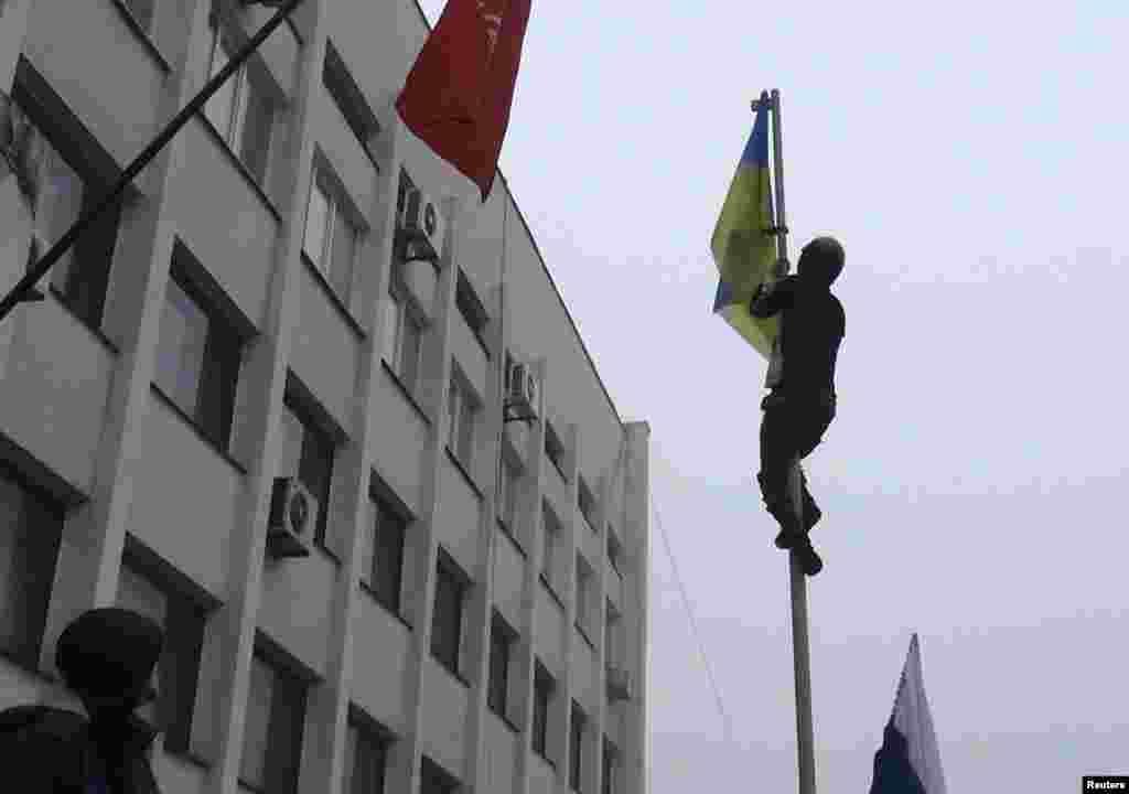 A man climbs a post to remove a Ukrainian flag as protesters hold a rally outside the mayor's office in Mariupol, April 13, 2014. 