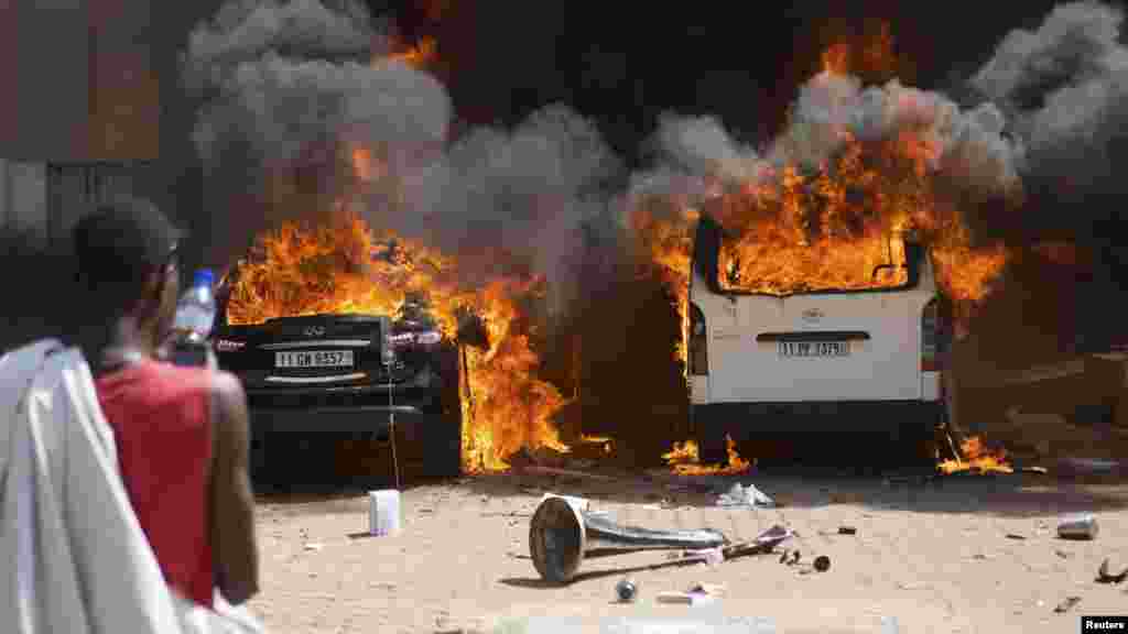 A man watches cars burn at a hotel where members of the parliament were said to be staying in Ouagadougou, capital of Burkina Faso, Oct. 30, 2014.