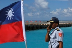 FILE - A member of the Taiwanese Coast Guard stands guard next to a Taiwanese flag on Itu Aba, which the Taiwanese call Taiping, at the South China Sea, Nov. 29, 2016.