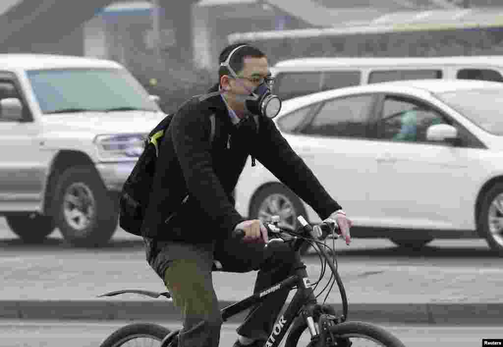 Seorang pria dengan mengenakan masker mengendarai sepeda pada suatu hari yang penuh asap polusi di Beijing, China.