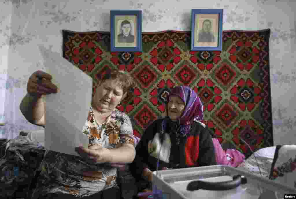 A local resident (right) listens before receiving a ballot during a parliamentary election inside her house in the village of Havronshchyna near Kyiv, Oct. 26, 2014.
