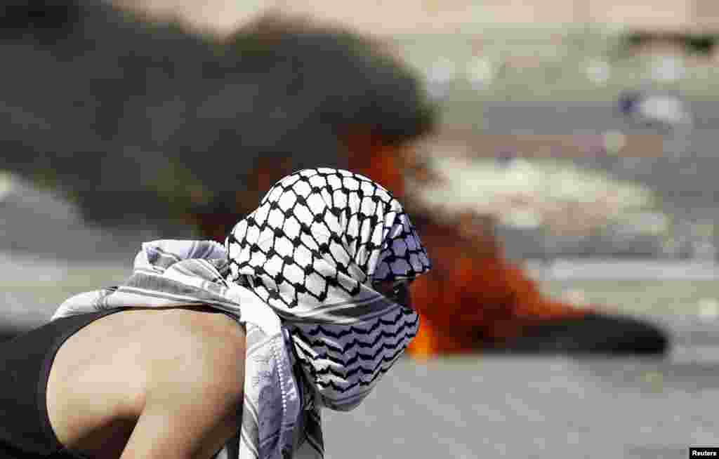 A Palestinian stone-thrower stands near a burning tire during clashes with Israeli police in Shuafat, an Arab suburb of Jerusalem, July 2, 2014.
