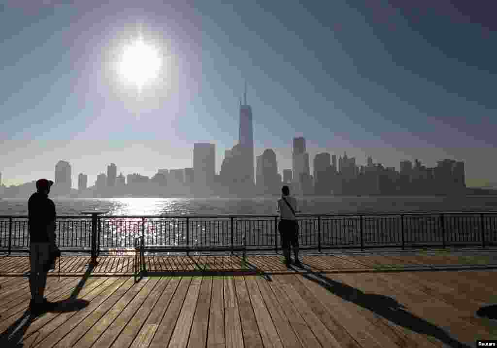 Dua orang di Jersey City, New Jersey, terlihat memandang cakrawala kota New York di seberang Sungai Hudson, setelah potongan terakhir, yang merupakan puncak dari One World Trade Center terpasang.