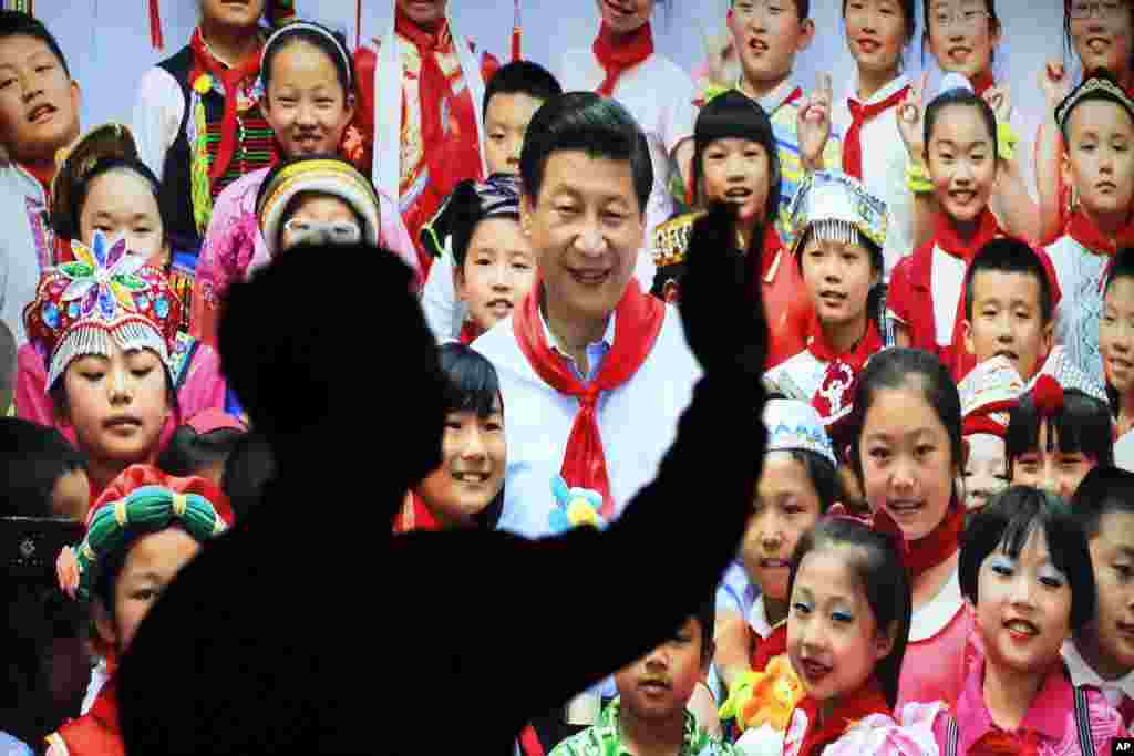 在十九大闭幕前一天,有人参观《砥砺奋进的五年》大型成就展,在一幅大型图片前面招手。图片上,中国主席习近平戴着少先队的红领巾和少年儿童合影(2017年10月23日)