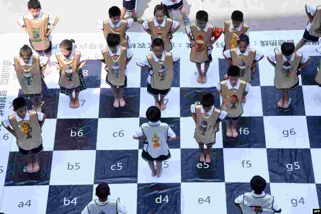 Children play chess on a giant chess board at a primary school in Handan in China's northern Hebei province. The "live" chess game was played by 32 students to promote chess at the school.