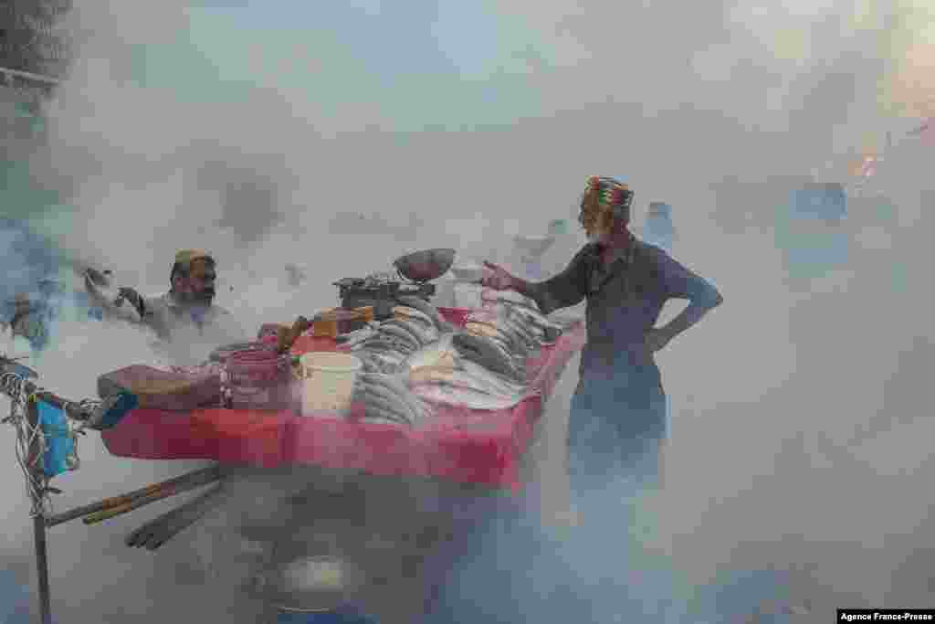 Vendors selling fish stand next to their cart duing a fumigation drive as a preventive measure against the disease-carrying mosquitoes, in Karachi, Pakistan, Oct. 26, 2021.