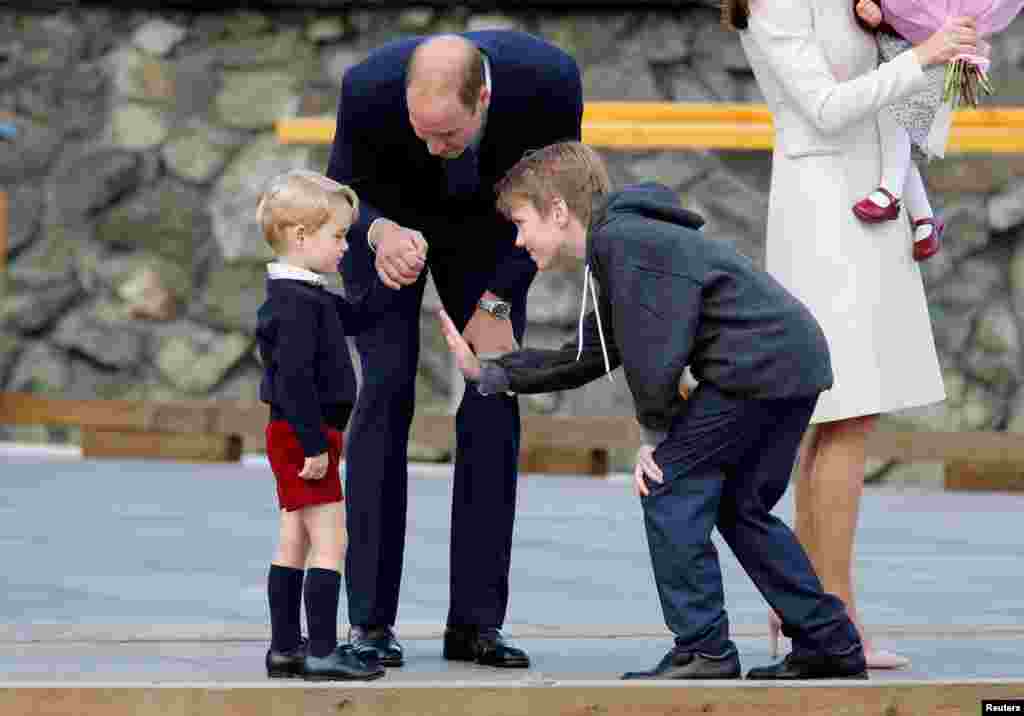 Daniel Bachman (R), who presented flowers to the Royal family, tries to high-five Britain's Prince George (L) while Prince William looks on as they arrive to board a floatplane for their official departure from Canada in Victoria, British Columbia, Canada, Oct. 1, 2016.