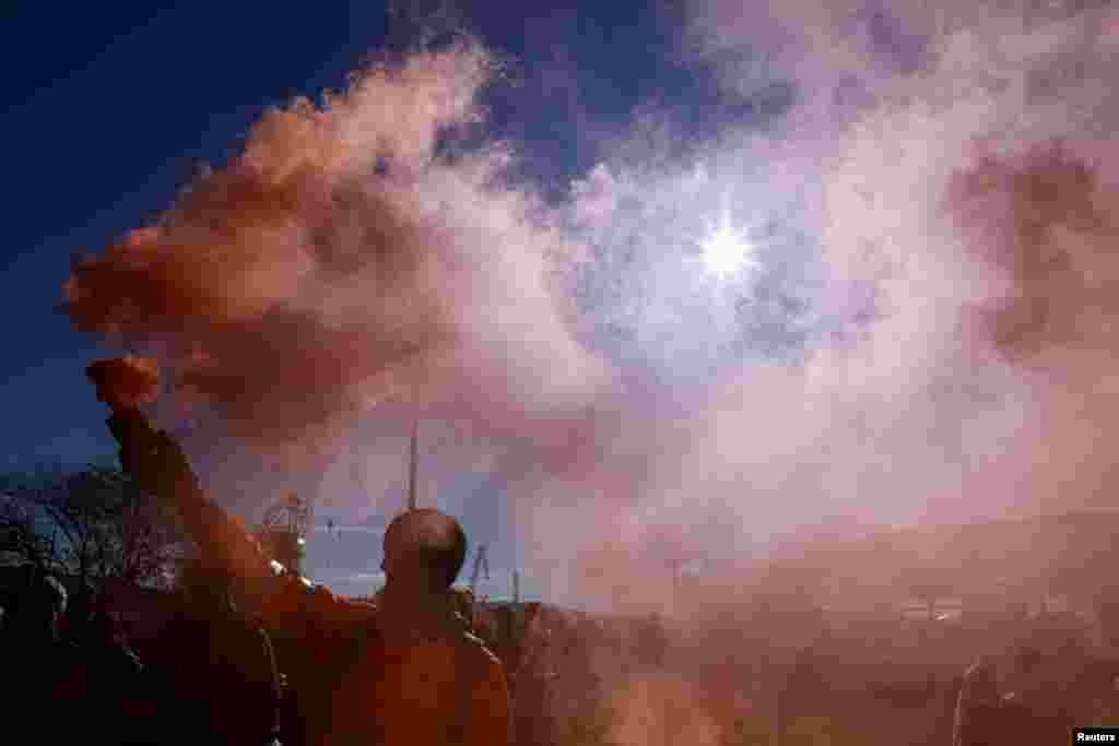 A person holds a flare as port workers gather outside the entrance of the major port of Trieste to protest the implementation of the COVID-19 health pass, the Green Pass, in the workplace, in Trieste, Italy.