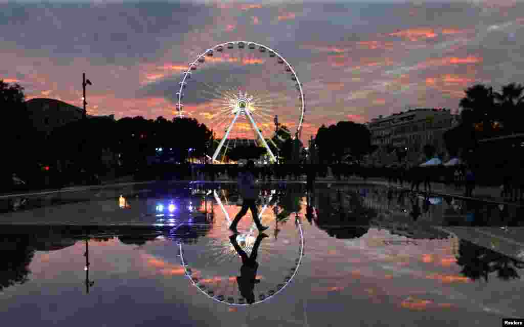 Bayangan dari seorang pria dan wahana hiburan kereta gantung "Ferris wheel" di kota Nice, Perancis.