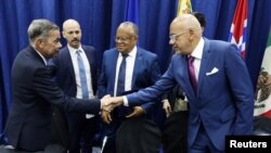 Los jefes de las delegaciones negociadoras de Venezuela, Gerardo Blyde (izquierda) y Jorge Rodríguez (derecha), se saludan frente a delegados internacionales en Barbados, durante la firma de acuerdos políticos, el martes 17 de octubre de 2023.