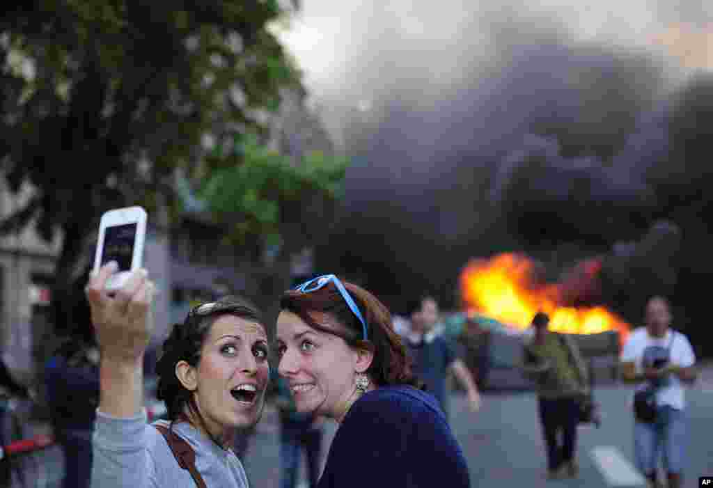 Wisatawan mengambil foto"selfie" ketika para demonstrator membakar sebuah tempat sampah dalam rally May Day di Barcelona, Spanyol, 1 Mei 2014. 