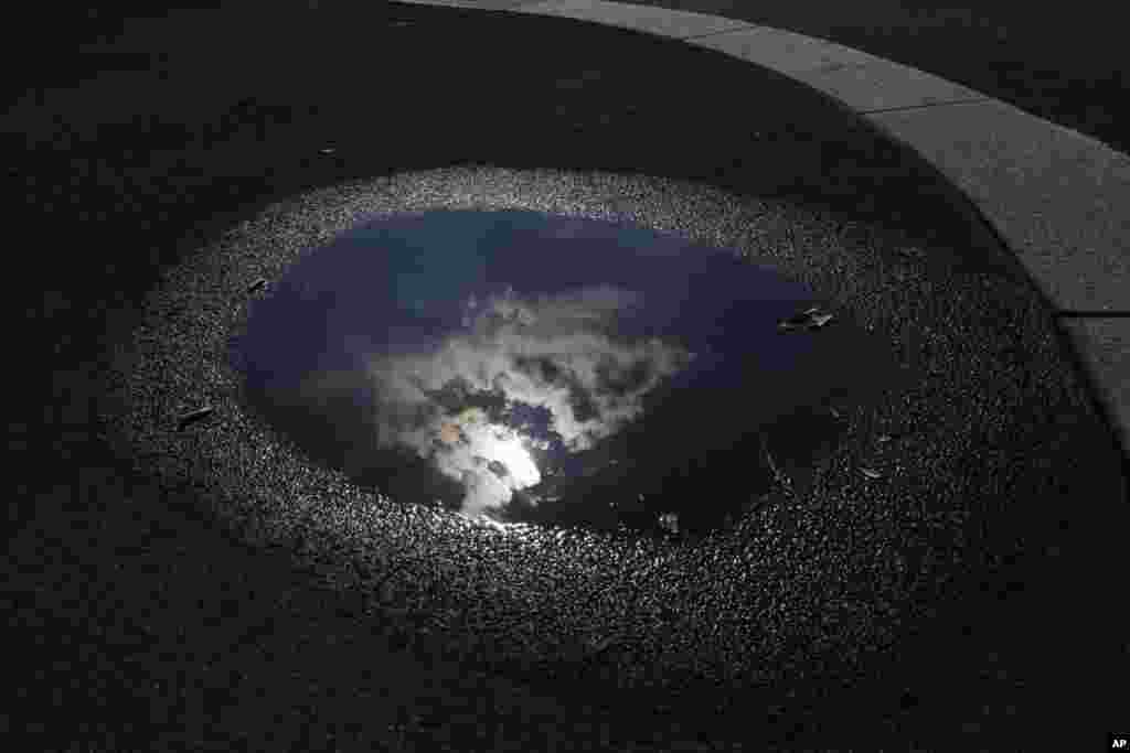 The sun and clouds are reflected in a puddle on a street in Milan, Italy.
