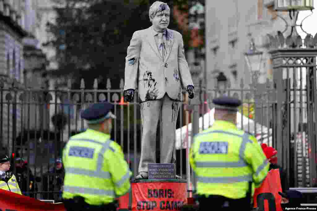 Police officers stand guard as Greenpeace activists stage a sit-in after installing an oil-splattered statue of British Prime Minister Boris Johnson by artist Hugo Farmer at Downing Street in London during a protest against the Cambo oil field project in the Shetland Islands.