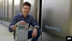 Joe Tavi, Bloom Energy senior director of manufacturing, holds a refurbished ventilator as he kneels beside fuel cells, April 1, 2020, in Sunnyvale, Calif.
