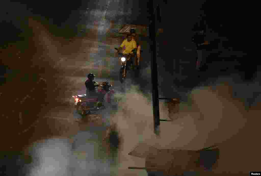 Men on motorcycles look at firefighters extinguishing motorcycles set ablaze by anti-government demonstrators at Altamira Square in Caracas, Feb. 26, 2014. 