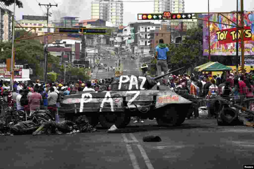Opposition supporters stand over a monument of a tank which they dragged into the middle of the street during a protest against Nicolas Maduro's government in San Cristobal, Venezuela, Feb. 19, 2014.