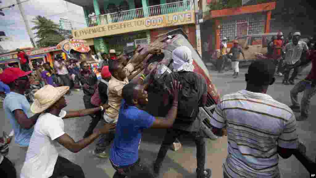 Demonstrators flip a car to block off a street during a protest demanding the resignation of President Michel Martelly in Port-au-Prince, Haiti, Jan. 11, 2015.