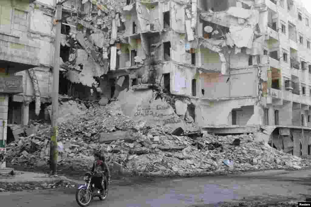 People ride on a motorbike past damaged buildings in Bustan al-Basha district in Aleppo, Syria, April 6, 2014.