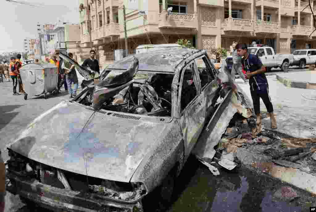 People inspect a car destroyed in a car bomb attack close to one of the main gates to the heavily-fortified Green Zone in Baghdad, Iraq, March 19, 2013.