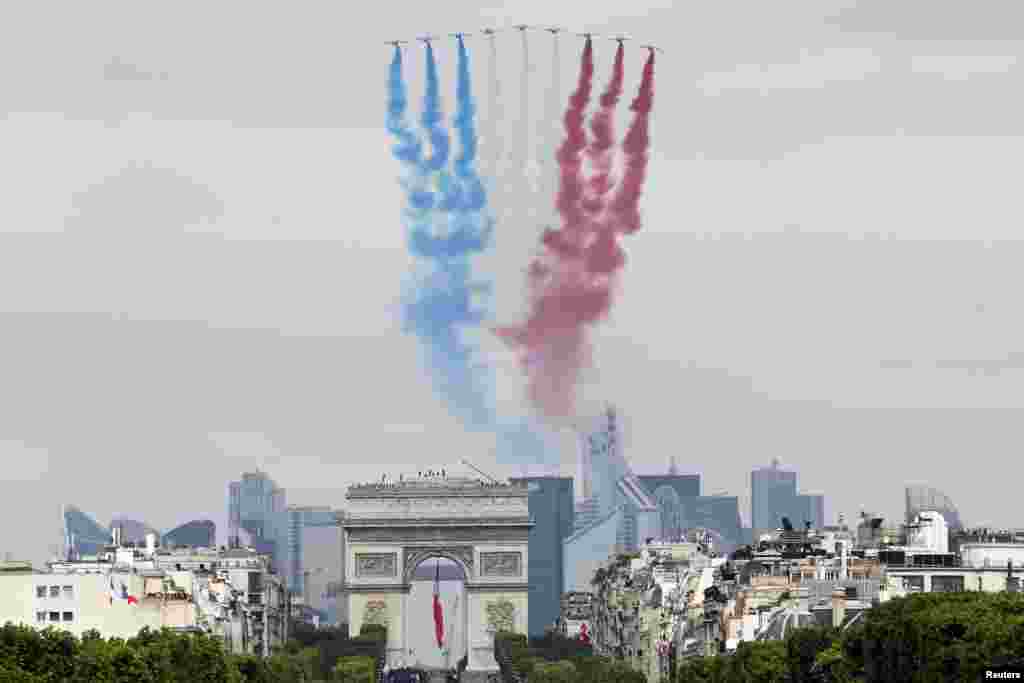 Sembilan jet alpha milik Angkatan Udara Perancis melepaskan asap dengan warna-warna nasional saat terbang di atas Arc de Triomphe dan Champs-Elysees selama parade militer Hari Bastille di Paris (14/7). (Reuters/Thomas Samson)