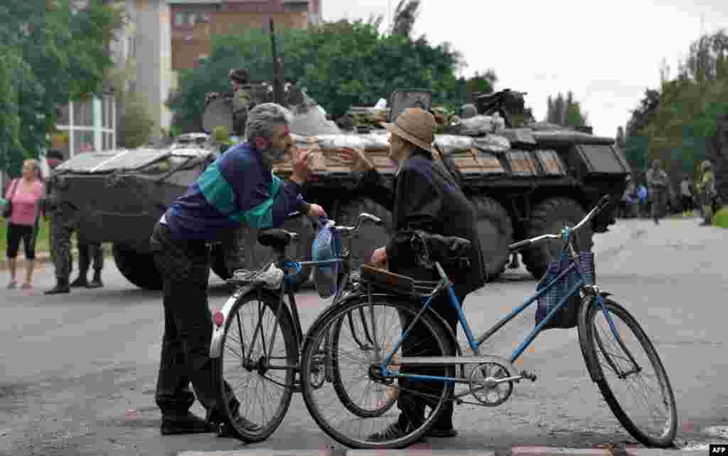 Warga di Slovyansk, Ukraina timur berbicara sementara tentara Ukraina siaga di belakang mereka.