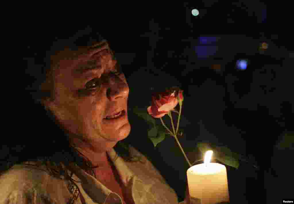 A woman cries as she holds a candle and a flower outside former South African President Nelson Mandela's house in Houghton, Dec. 5, 2013a