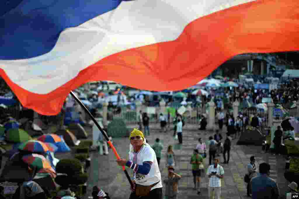 Seorang pengunjuk rasa anti-pemerintah di Thailand melambaikan bendera nasional Thailand dalam unjuk rasa yang berkelanjutan di lokasi demonstrasi di Victory Monument di pusat kota Bangkok. Keputusan pengadilan untuk mengembalikan kepada pemerintah dan komisi pemilihan untuk memutuskan apakah pemilu akan ditunda atau tidak karena adanya kerusuhan yang mematikan, menyebabkan pemilihan yang kontroversial itu berada dalam ketidakpastian.