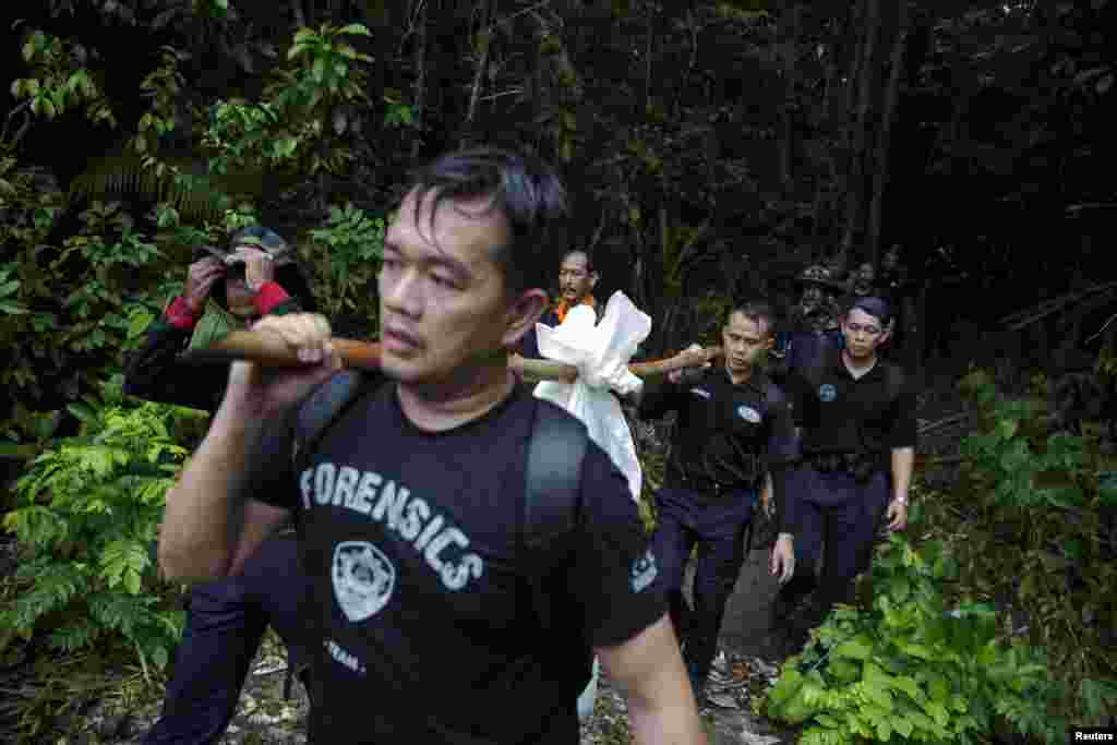 Tim forensik polisi mengangkut kantung jenazah berisi sisa-sisa mayat manusia yang digali dari kuburan dekat kamp perdagangan manusia yang ditelantarkan di hutan dekat perbatasan Thailand di Bukit Wang Burma, Malaysia utara (27/5). (Reuters/Damir Sagolj)