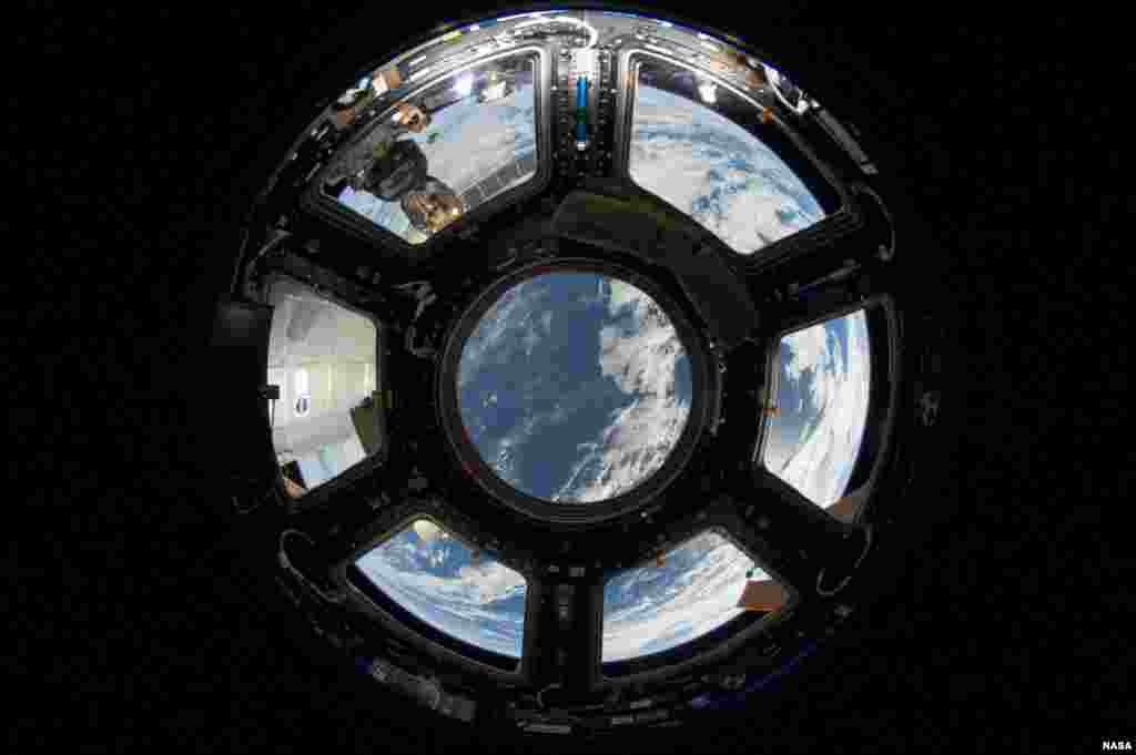 A view of Earth as seen from the Cupola on the Earth-facing side of the International Space Station. Visible in the top left foreground is a Russian Soyuz crew capsule. A solar array panel can be seen in the lower right corner.