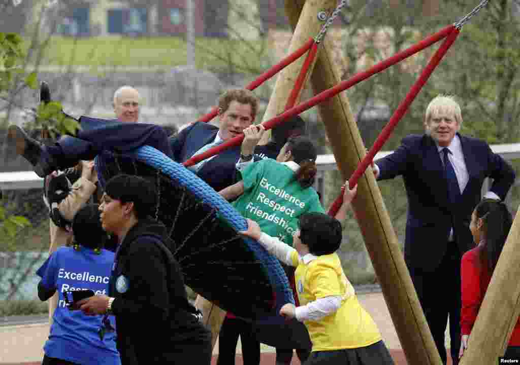 Pangeran Harry dari Inggris bermain ayunan dengan anak-anak sementara walikota London Boris Johnson (kanan) mengamati mereka, dalam sebuah acara kunjungan ke Taman Olimpik Ratu Elizabeth sebelum pembukaan taman itu pada tanggal 5 April 2014, di Stratford di London Timur. 