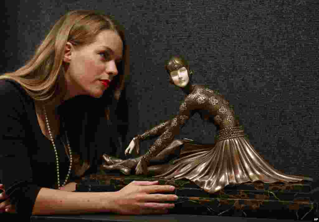 A Bonhams employee poses with a bronze and ivory sculpture 'Tanara' by Demetre Chiparus on display at the auction house in London, June 17, 2013. The sculpture is to be auctioned in 20th Century Decorative Arts sale on June 19 with an estimated price of 25,000 to 30,000 pounds (US$ 39,302 to 47,151 or 29,460 to 35,345 euro).