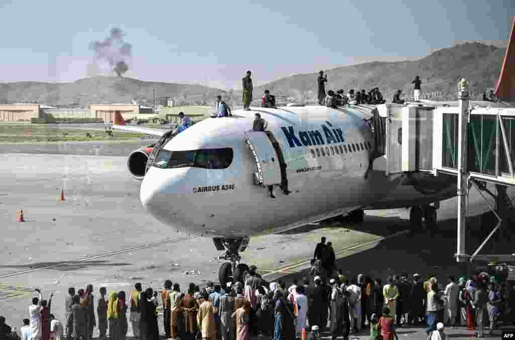 Afghan people climb atop a plane as they wait at the Kabul airport in Kabul.