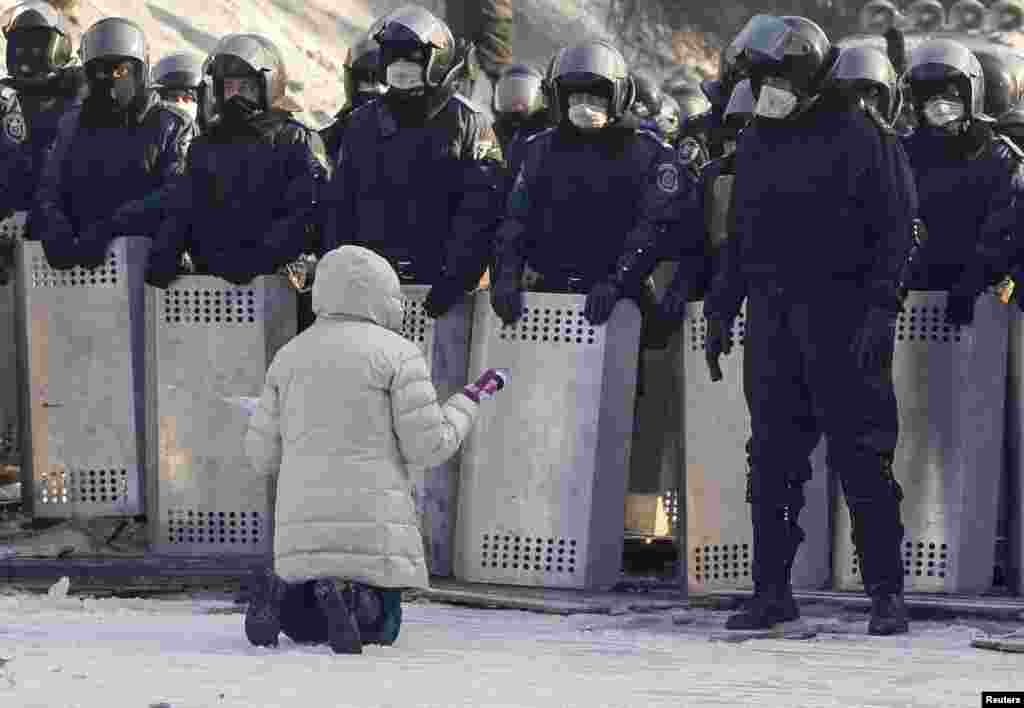 Seorang perempuan bersimpuh memohon kepada pasukan polisi Ukraina di lokasi bentrokan dengan para demonstran anti-pemerintah di Kiev. Para pengunjuk rasa mendirikan lebih banyak barikade di jalan dan menduduki sebuah gedung pemerintah pada hari Jumat setelah perundingan gagal mencapai kesepakatan.