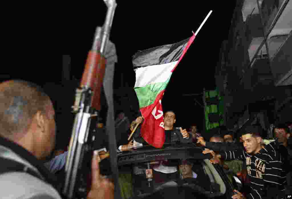 Seorang pria Palestina menembakkan senjata ke udara sementara yang lainnya berkumpul mengelilingi seorang tahanan Palestina yang dibebaskan, Omar Masoud, pada saat kedatangannya di rumah keluarganya di Kamp Pengungsi Shati (30/10). (AP/Adel Hana)