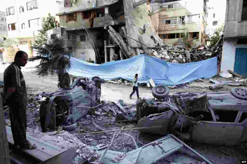 Palestinians look at damaged cars amid the rubble of destroyed buildings following an Israeli air strike on July 14, 2014 in Gaza City.