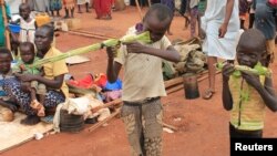 FILE - Martin Andrea, 10, and a friend play with toy guns made from long grass reeds at a displaced persons camp protected by U.N. peacekeepers in Wau, South Sudan.